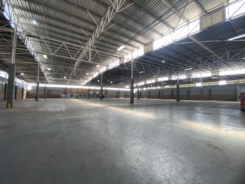 Expansive industrial warehouse space featuring high ceilings with exposed steel trusses, concrete flooring, and ample natural light through clerestory windows.