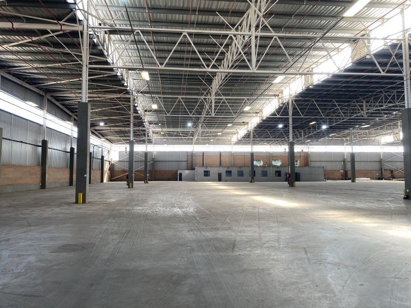 Expansive industrial warehouse space featuring high ceilings with exposed steel trusses, concrete flooring, and an integrated internal office structure.