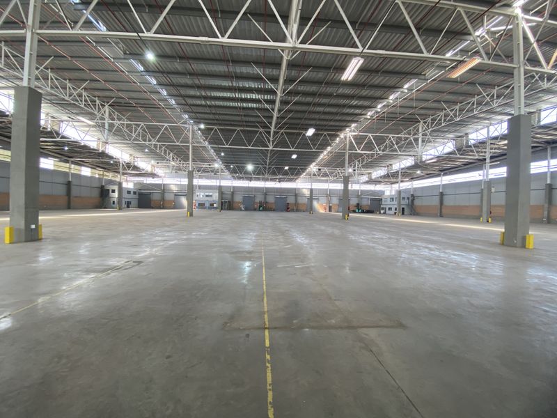 A vast, open-plan industrial warehouse space featuring high ceilings with exposed steel trusses, polished concrete flooring, and ample natural light.