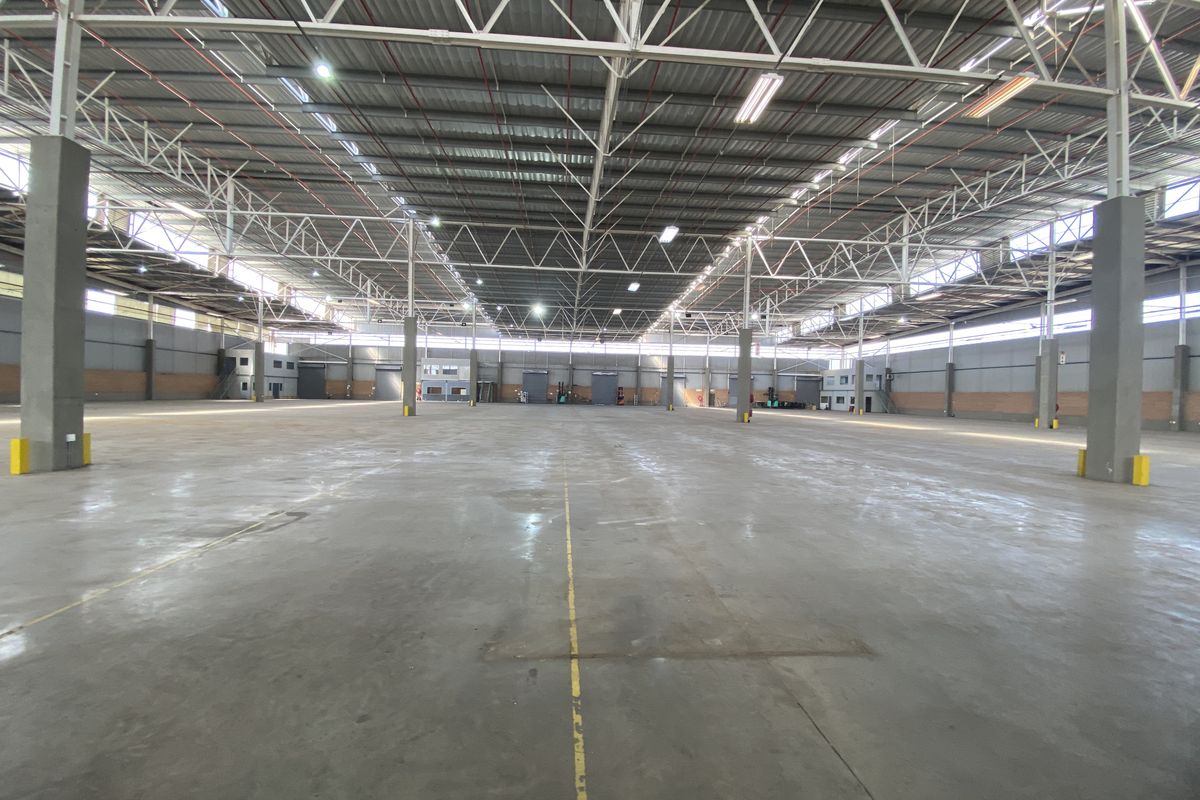 A vast, open-plan industrial warehouse space featuring high ceilings with exposed steel trusses, polished concrete flooring, and ample natural light.