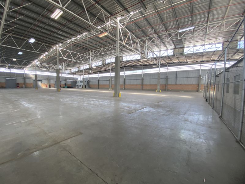 Expansive industrial warehouse space featuring high-clearance steel truss roofing, polished concrete flooring, and secure chain link partitioning.