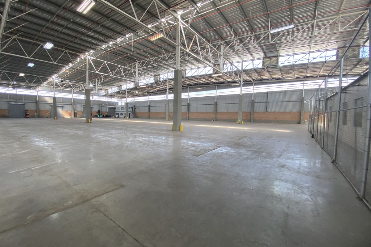 Expansive industrial warehouse space featuring high-clearance steel truss roofing, polished concrete flooring, and secure chain link partitioning.