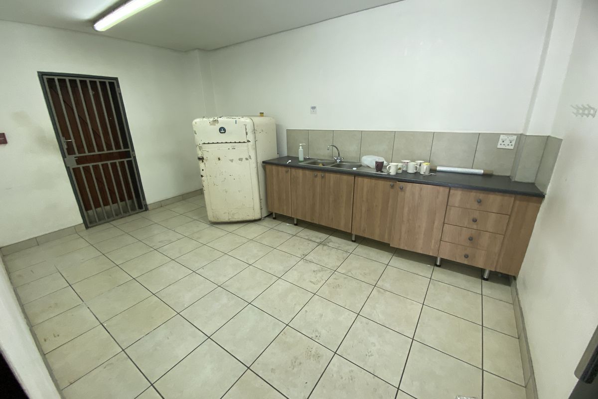 A functional industrial kitchen area featuring built-in cabinetry, a stainless steel sink, tiled flooring, and a secure metal entrance gate.