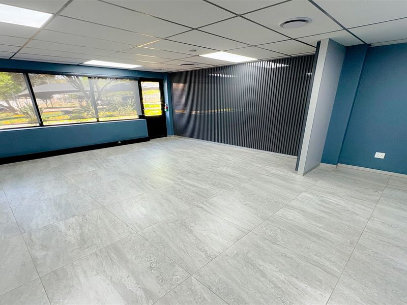 A bright, modern, and empty office space featuring large windows, contemporary tiled flooring, a decorative slatted feature wall, and a suspended ceiling with recessed lighting.