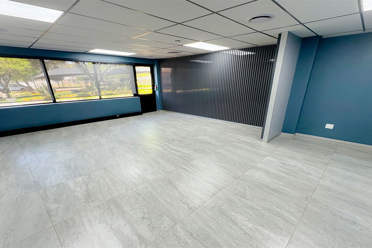 A bright, modern, and empty office space featuring large windows, contemporary tiled flooring, a decorative slatted feature wall, and a suspended ceiling with recessed lighting.