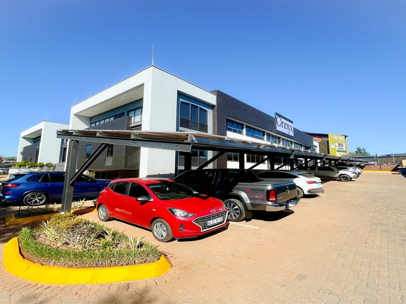 Modern office building exterior featuring a paved parking area with covered bays and well-maintained landscaped garden beds.