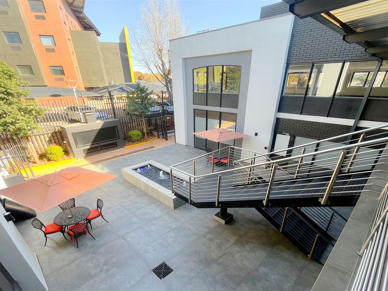 Modern outdoor courtyard featuring a tiled patio, built-in fireplace, water feature, and a contemporary metal staircase with stainless steel railings.