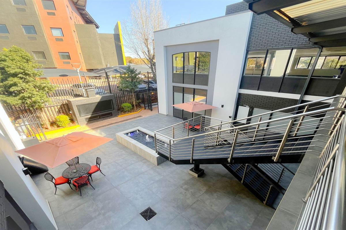 Modern outdoor courtyard featuring a tiled patio, built-in fireplace, water feature, and a contemporary metal staircase with stainless steel railings.