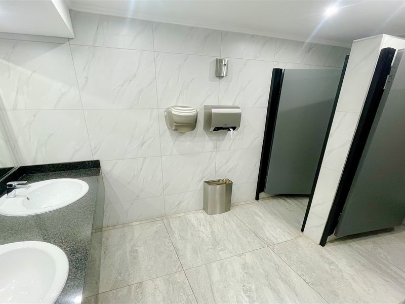 Modern commercial bathroom featuring dual vanity sinks with granite countertops, tiled finishes, and partitioned toilet stalls for professional office use.