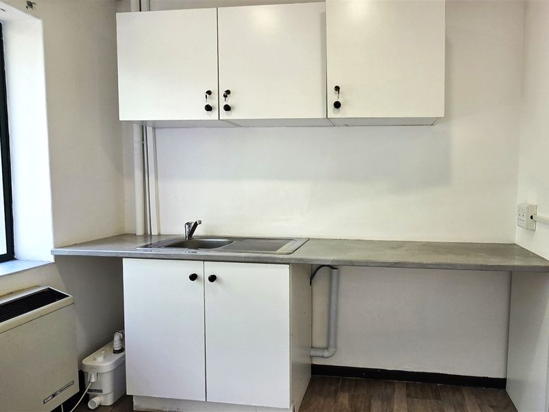 A functional office kitchenette featuring white built-in cabinetry, a stainless steel sink, laminate countertop, and a large window providing natural light.