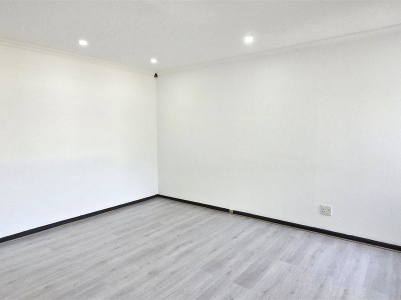 A bright, empty office space featuring modern laminate flooring, recessed ceiling lighting, and a wall-mounted HVAC unit.