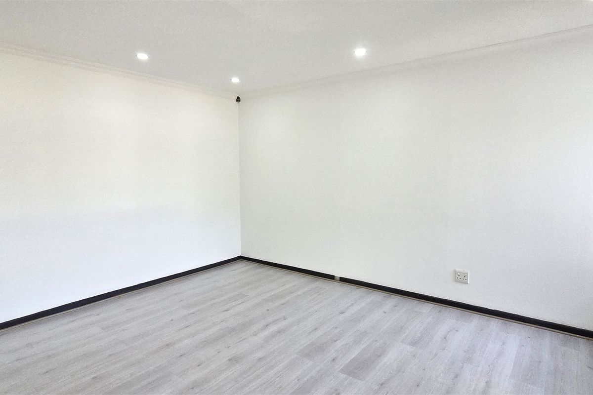 A bright, empty office space featuring modern laminate flooring, recessed ceiling lighting, and a wall-mounted HVAC unit.