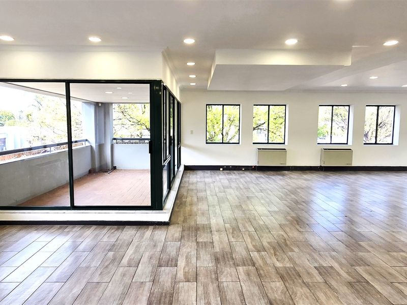 Spacious, open-plan office area featuring wood-look tile flooring, recessed lighting, multiple windows for natural light, and direct access to a private balcony.