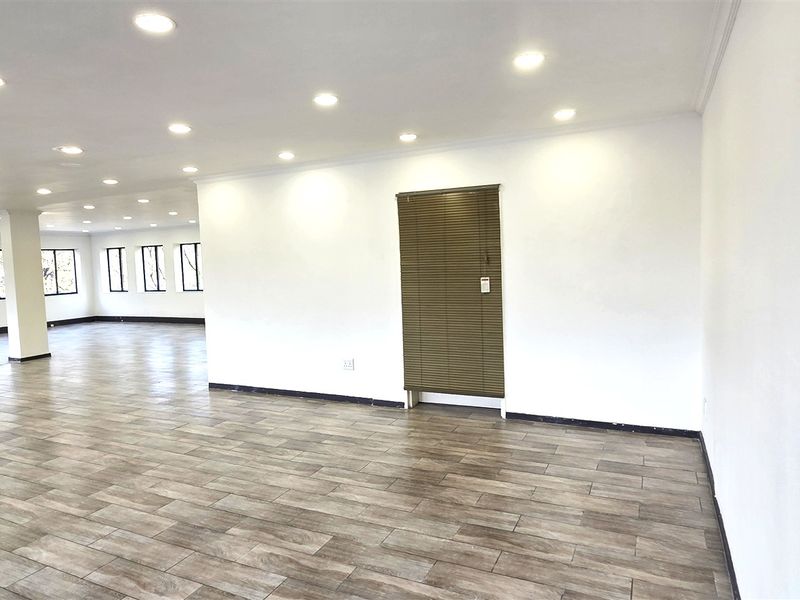 Spacious open-plan office area featuring modern tiled flooring, recessed ceiling lighting, and large windows providing ample natural light.