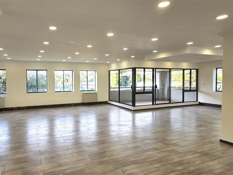 Spacious, open-plan office area featuring modern tiled flooring, recessed downlighting, and an integrated enclosed balcony, providing a bright and versatile workspace.