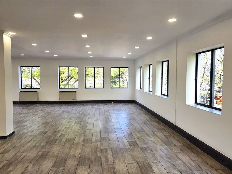 Spacious, open-plan office area featuring wood-look tile flooring, recessed downlights, and large windows providing ample natural light.