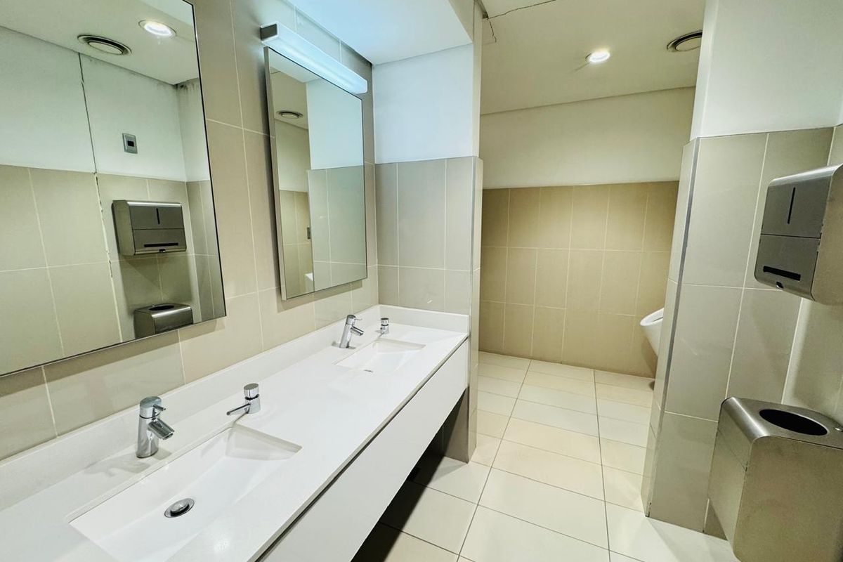 A clean, functional commercial office bathroom featuring a double vanity, tiled surfaces, and a separate urinal area.