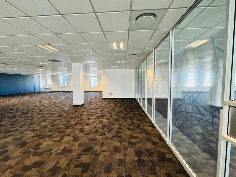 Spacious open-plan office area featuring modern glass partitions, suspended ceilings with recessed lighting, and durable carpet tiles throughout.