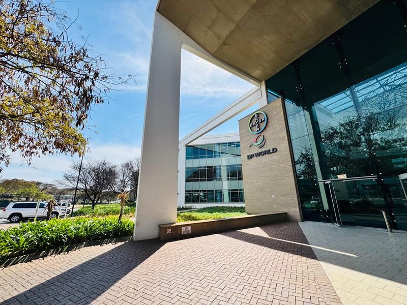 Modern office building entrance featuring a glass facade, stone cladding, and a paved approach with structural concrete architectural elements.