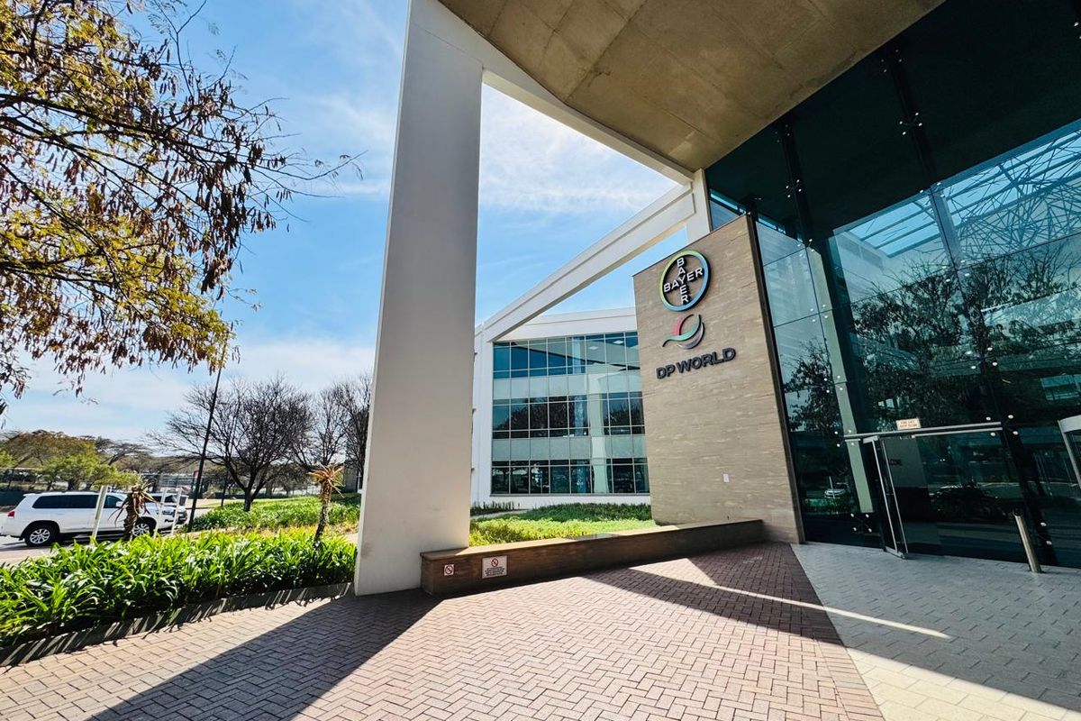 Modern office building entrance featuring a glass facade, stone cladding, and a paved approach with structural concrete architectural elements.