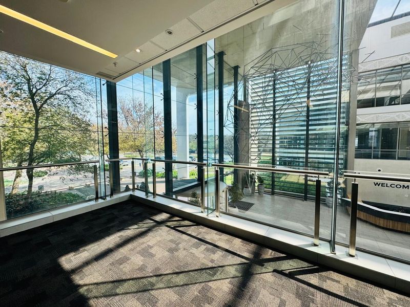 Modern office space featuring expansive floor-to-ceiling glass windows, stainless steel railings, and high-quality carpeted flooring with abundant natural light.