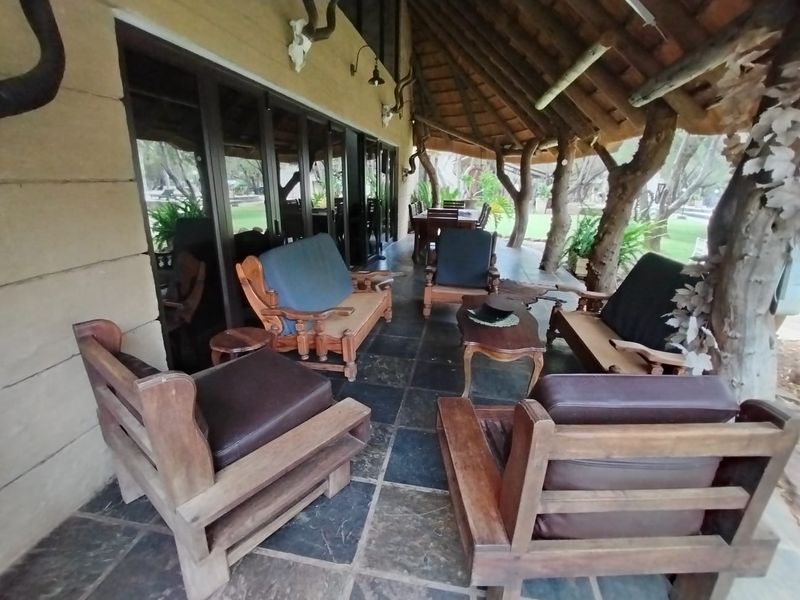 A covered outdoor patio area featuring a rustic thatched roof, stone tile flooring, and large sliding glass doors leading into the main living space.