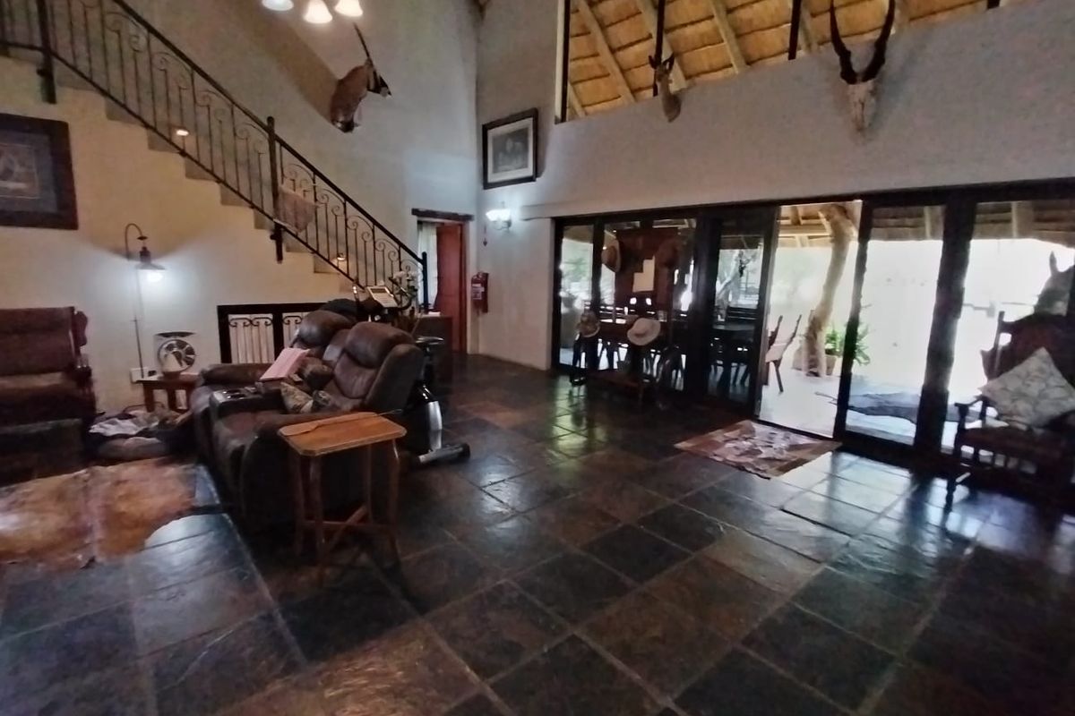 Spacious living area featuring slate flooring, a wrought iron staircase, and high vaulted ceilings with exposed thatch and timber rafters.
