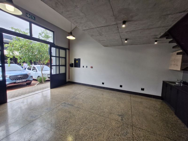 Modern open-plan retail or office space featuring polished concrete floors, exposed concrete ceilings, and a sleek kitchenette with direct access to the exterior.
