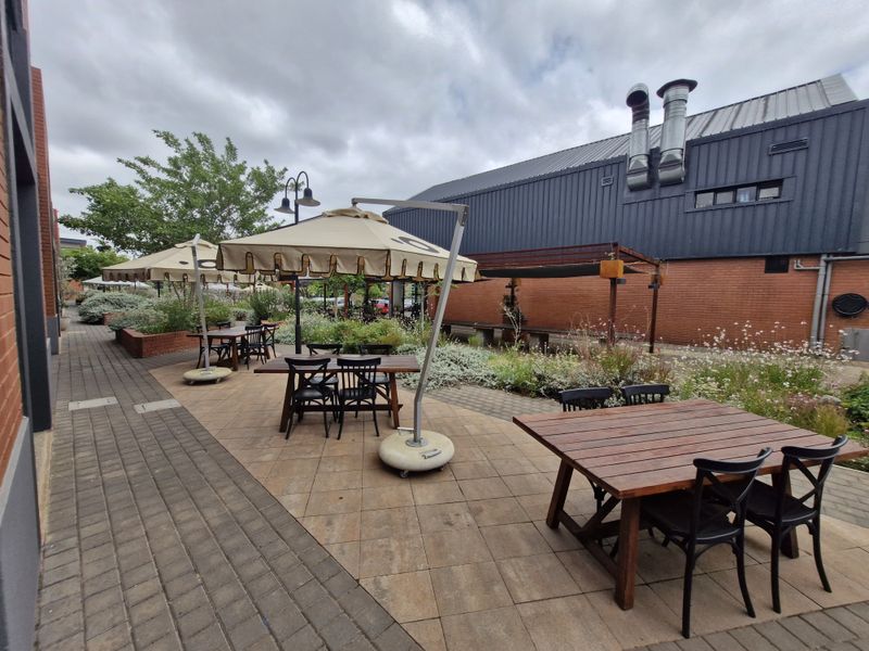 Outdoor patio area featuring paved flooring, raised brick planters, and industrial-style building exterior with prominent metal extractor flues.