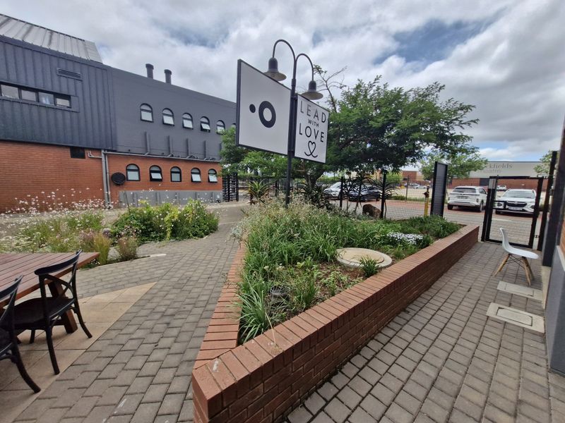 A well-maintained outdoor courtyard area featuring brick paving, a raised garden planter, and integrated signage with gooseneck lighting.