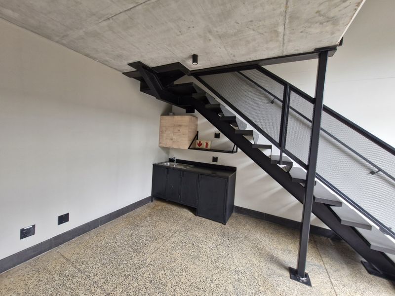 Modern utility space featuring an industrial aesthetic with an exposed concrete ceiling, polished concrete floors, and a sleek metal staircase with mesh balustrade.