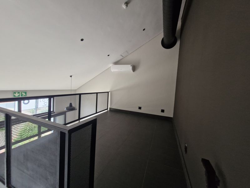 An open-plan mezzanine level featuring modern tiled flooring, a metal mesh balustrade, exposed ducting, and a wall-mounted split-system air conditioner.