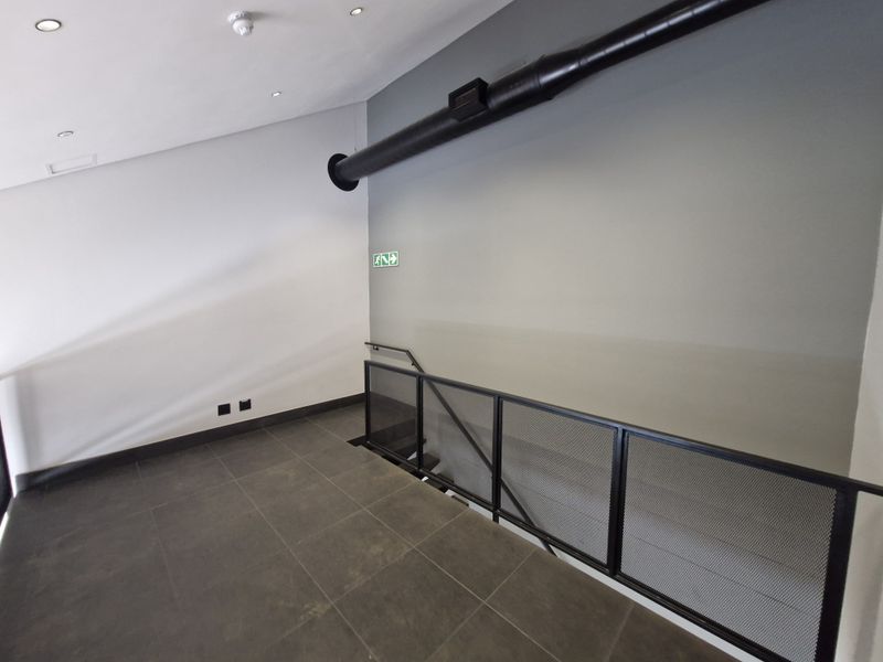 Modern hallway featuring industrial-style exposed ducting, sleek tiled flooring, and a contemporary black metal mesh balustrade overlooking the staircase.