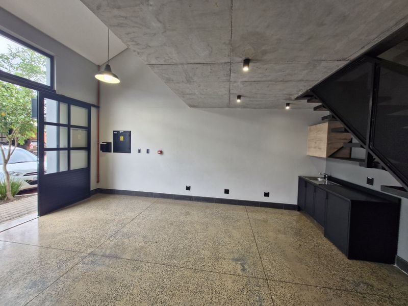 Modern open-plan retail or office space featuring polished concrete floors, exposed concrete ceiling, kitchenette, and a striking black metal staircase.