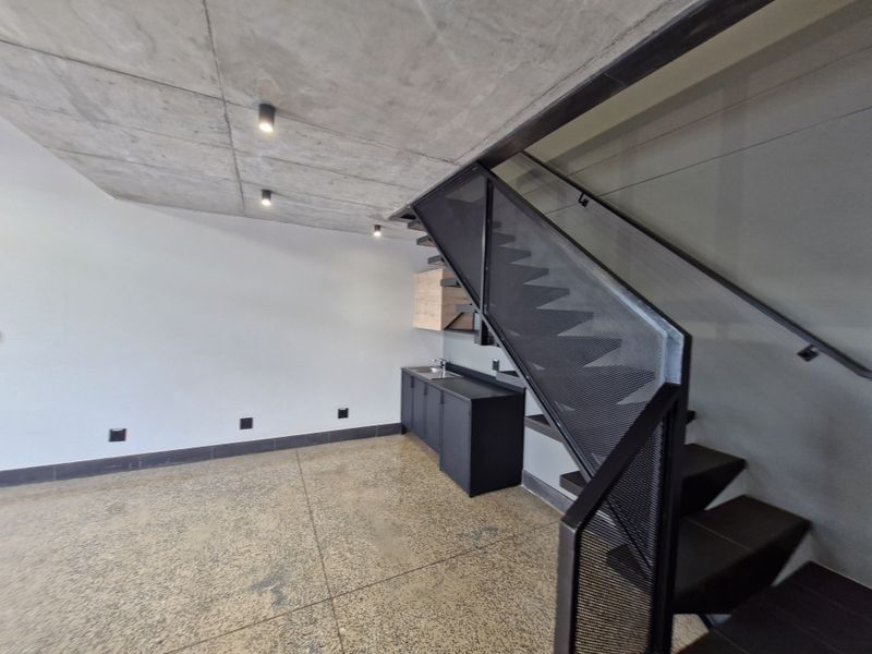 Modern open-plan retail space featuring polished concrete floors, an exposed concrete ceiling, and a sleek metal staircase with integrated kitchenette cabinetry.