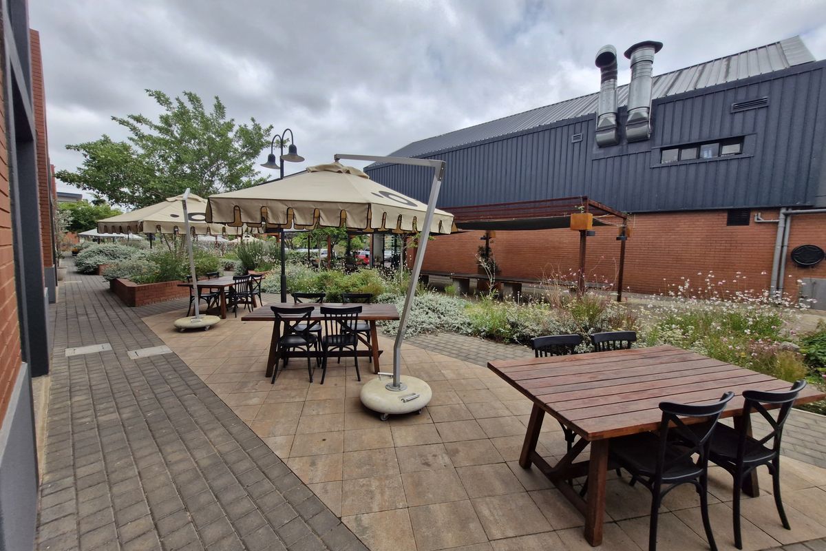 Outdoor patio area featuring paved flooring, raised brick planters, and industrial-style building exterior with prominent metal extractor flues.