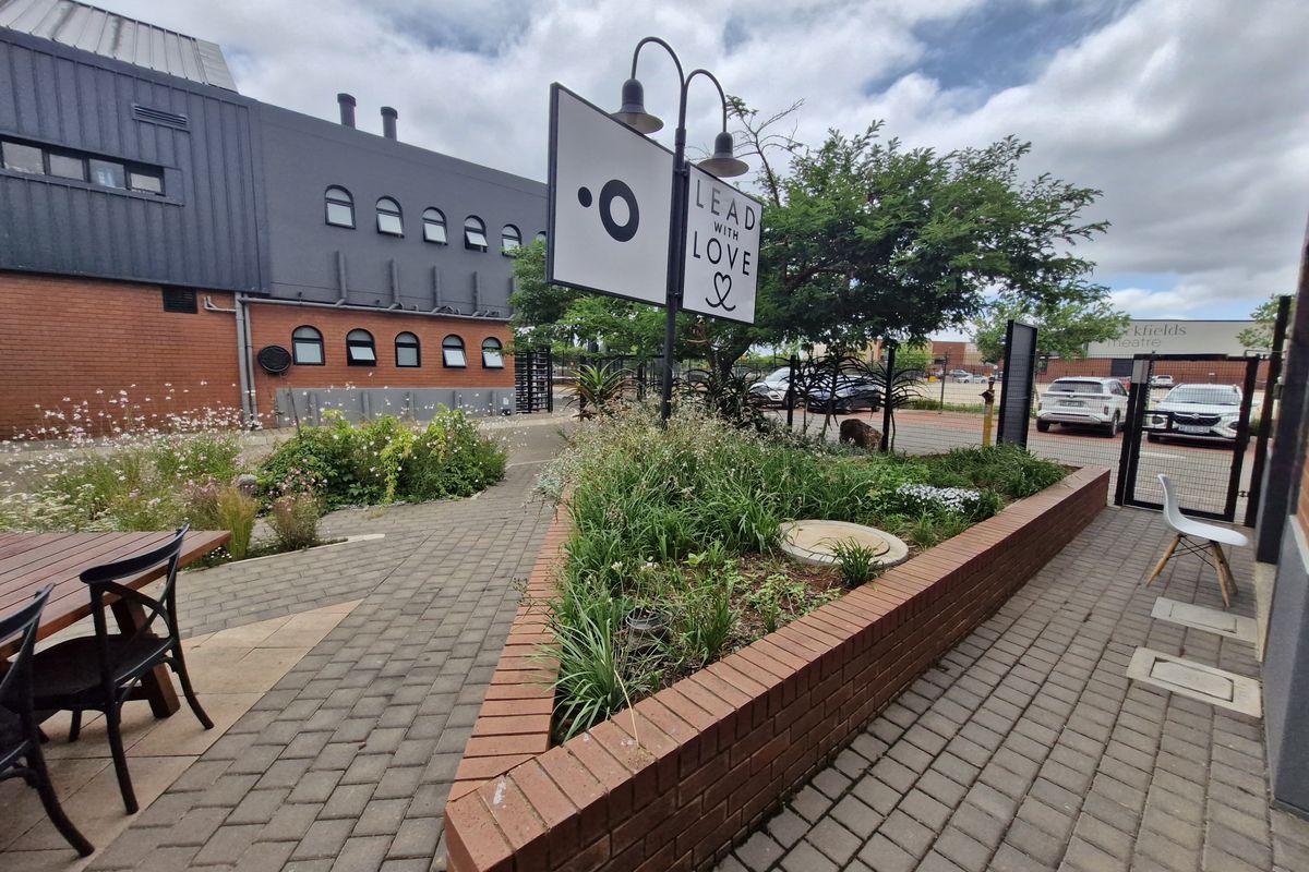 A well-maintained outdoor courtyard area featuring brick paving, a raised garden planter, and integrated signage with gooseneck lighting.