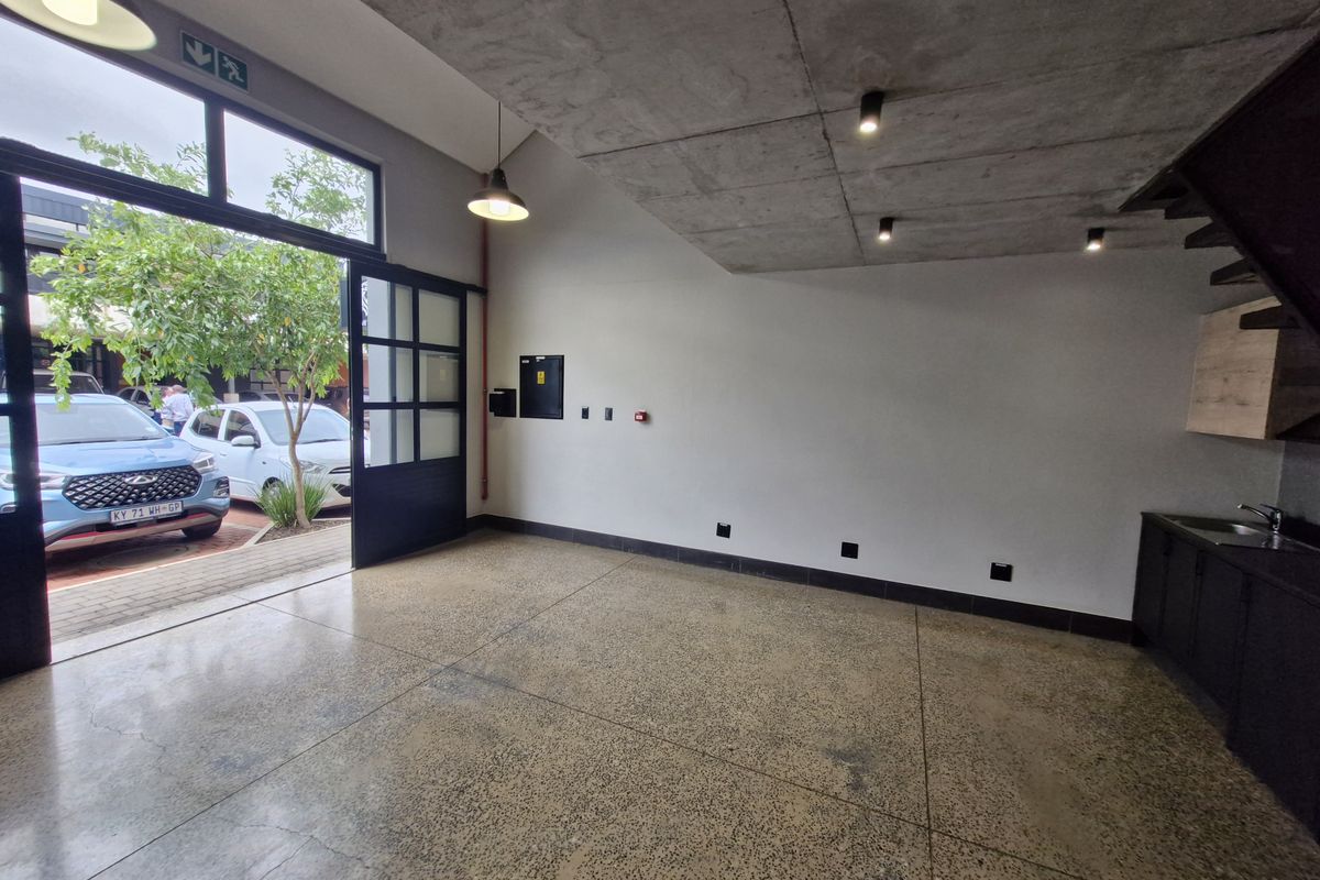 Modern open-plan retail or office space featuring polished concrete floors, exposed concrete ceilings, and a sleek kitchenette with direct access to the exterior.