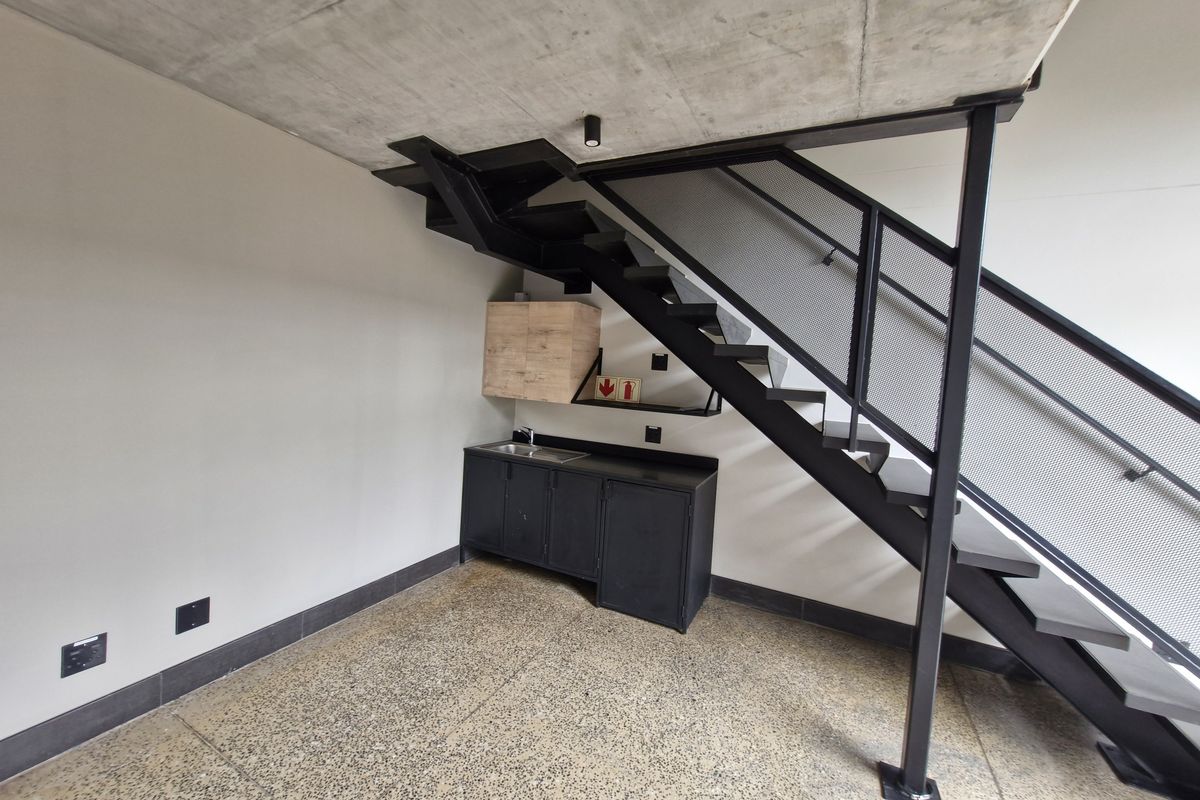 Modern utility space featuring an industrial aesthetic with an exposed concrete ceiling, polished concrete floors, and a sleek metal staircase with mesh balustrade.