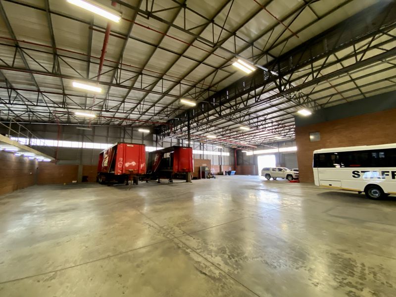 Spacious industrial warehouse featuring high ceilings with exposed steel trusses, concrete flooring, and integrated fire sprinkler systems.