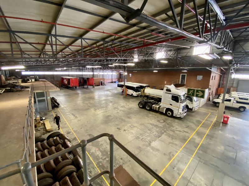 Spacious industrial warehouse featuring high ceilings with exposed steel trusses, concrete flooring, and a mezzanine level, suitable for logistics or storage operations.