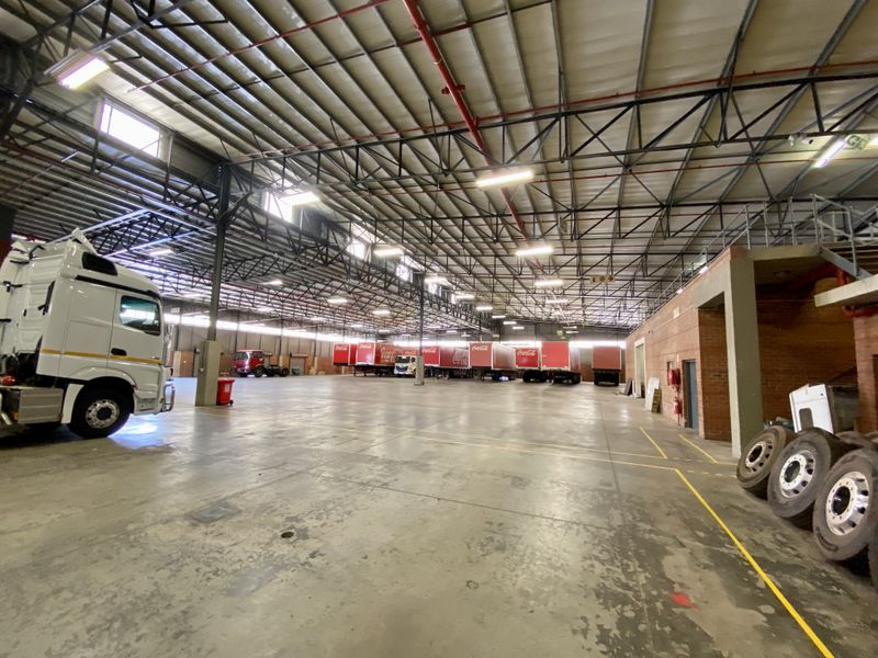 Spacious industrial warehouse facility featuring high ceilings with exposed steel trusses, concrete flooring, and integrated fire sprinkler systems.
