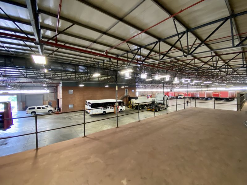 Large industrial warehouse space featuring high exposed steel roof trusses, fire sprinkler systems, and expansive concrete flooring suitable for logistics or manufacturing operations.