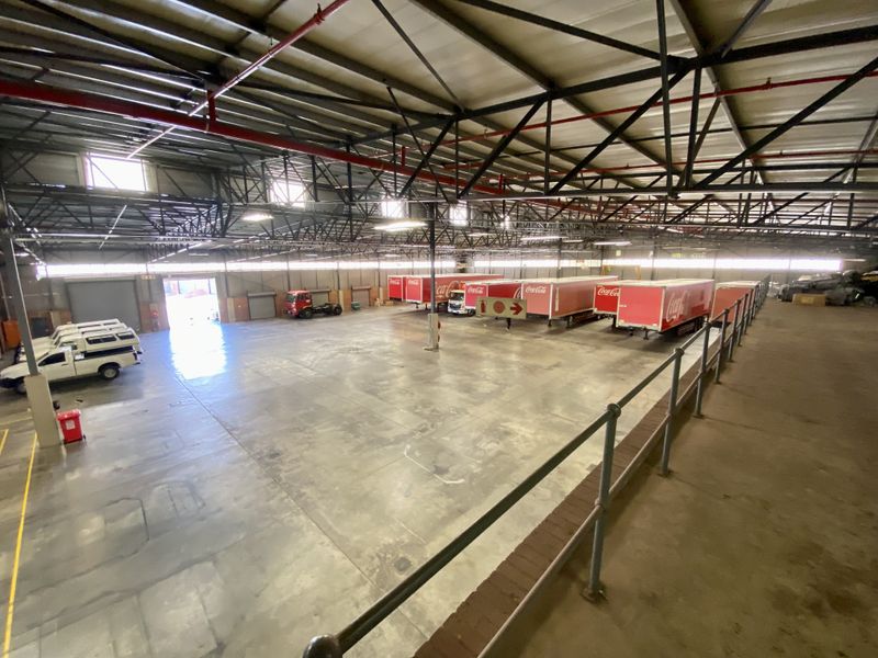 Spacious industrial warehouse featuring high-clearance steel roof trusses, concrete flooring, and multiple roller shutter doors for efficient loading and logistics operations.