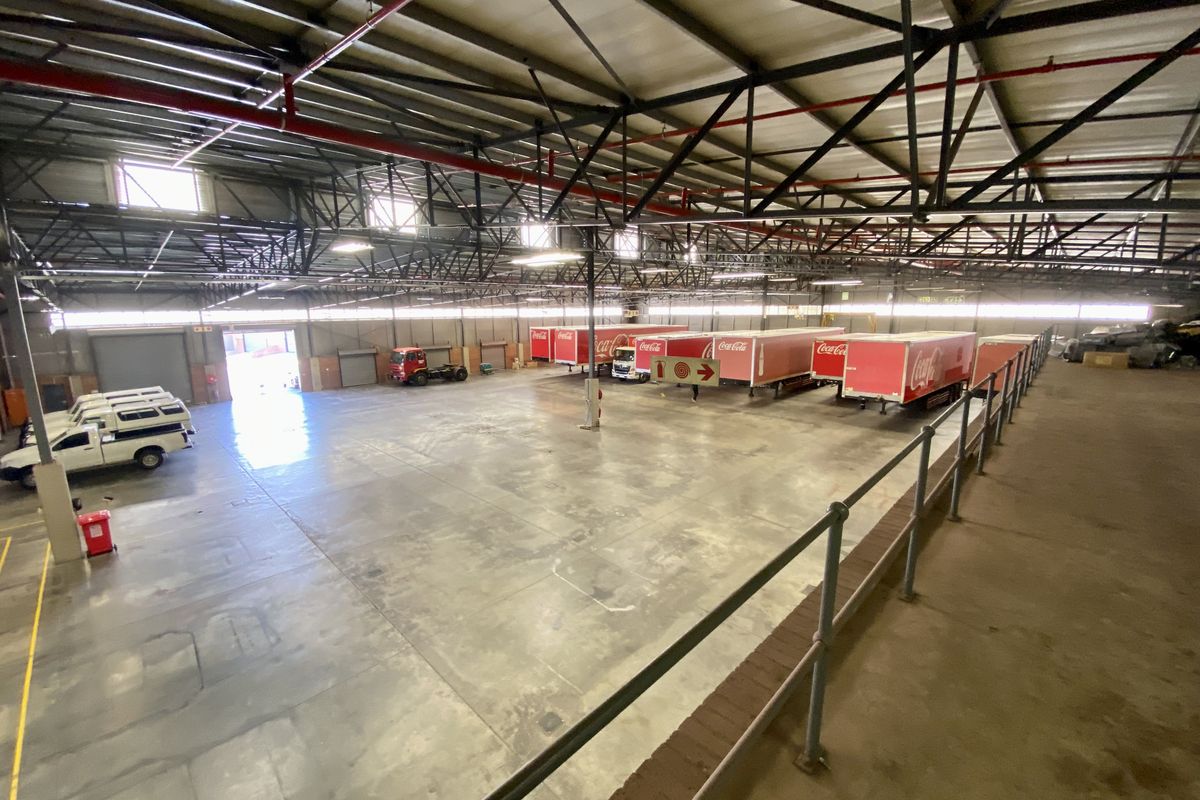 Spacious industrial warehouse featuring high-clearance steel roof trusses, concrete flooring, and multiple roller shutter doors for efficient loading and logistics operations.