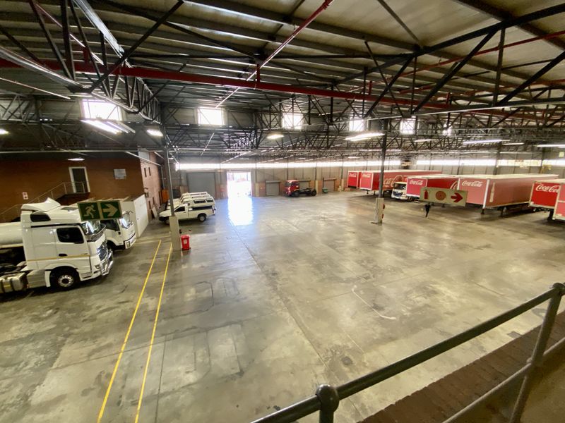 Large industrial warehouse space featuring high-clearance steel roof trusses, fire sprinkler systems, and expansive concrete flooring suitable for logistics or manufacturing operations.