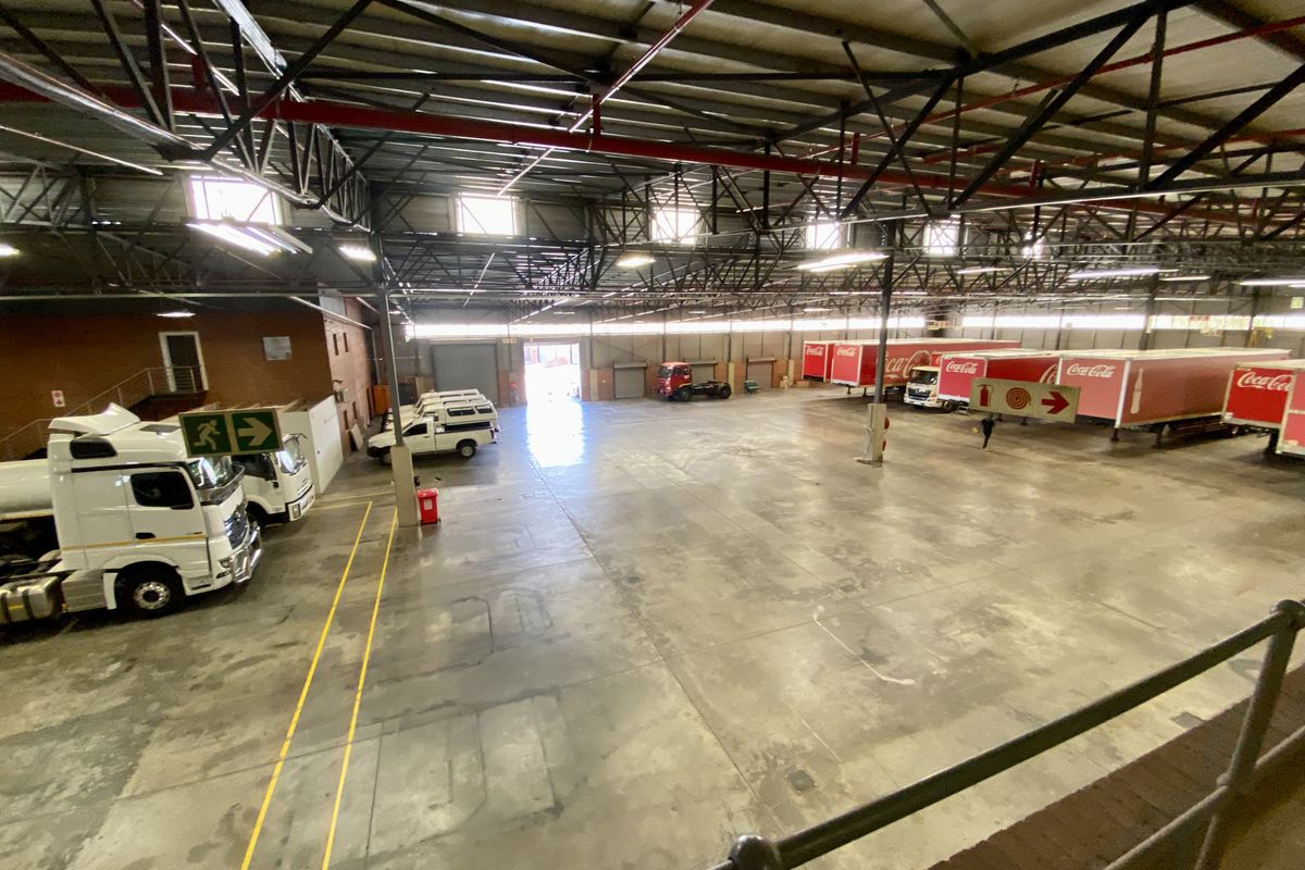 Large industrial warehouse space featuring high-clearance steel roof trusses, fire sprinkler systems, and expansive concrete flooring suitable for logistics or manufacturing operations.