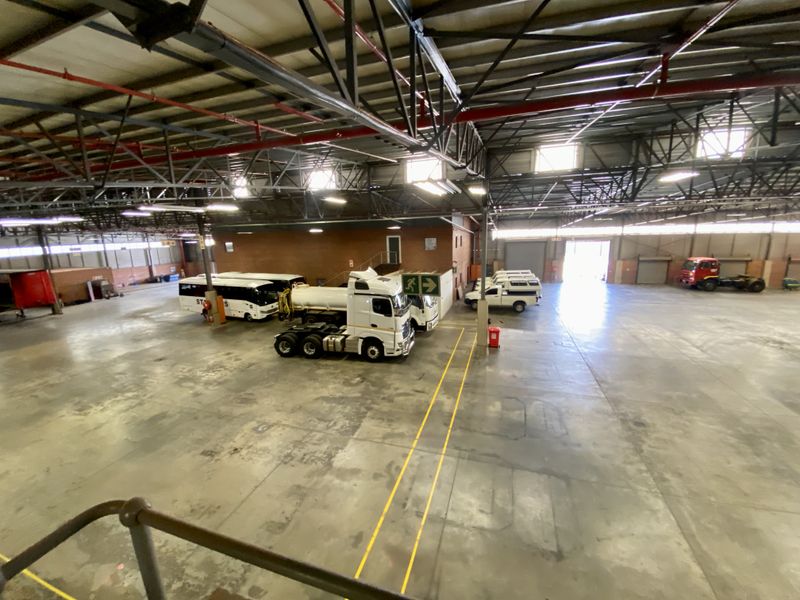 Spacious industrial warehouse featuring high ceilings with exposed steel trusses, concrete flooring, fire sprinkler systems, and large roller shutter access doors.