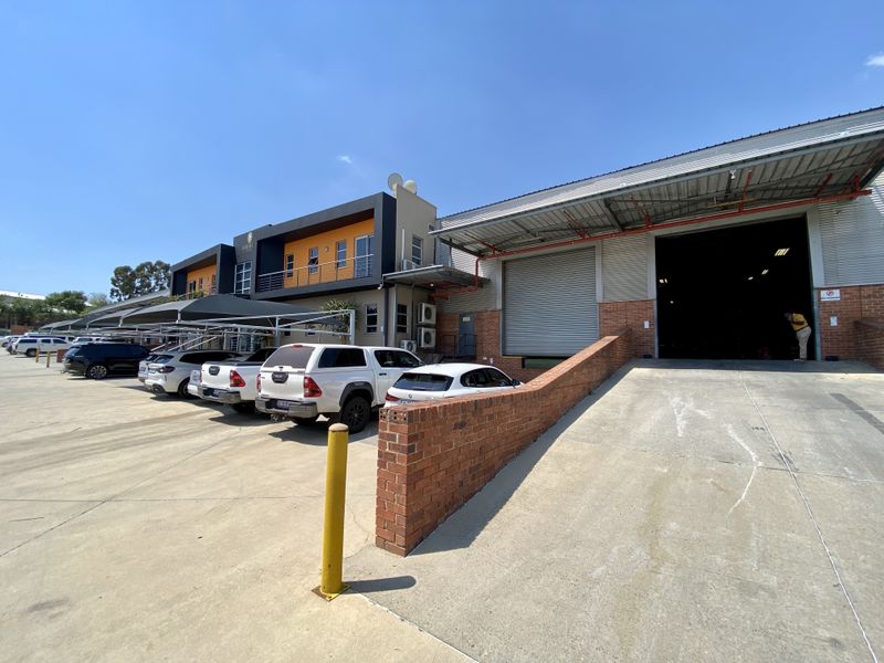 Industrial property featuring a large roller shutter door, loading ramp, and dedicated parking area with carports.