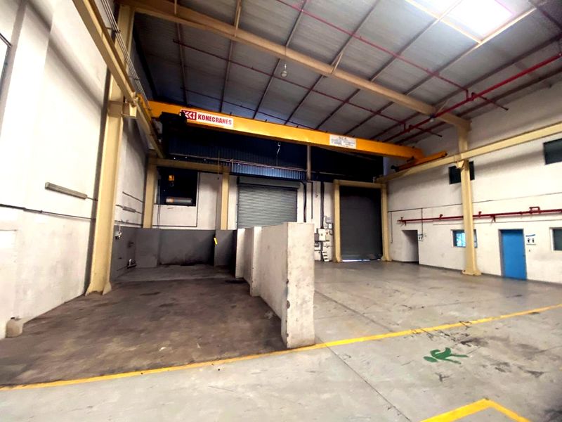 Spacious industrial warehouse featuring a high-clearance overhead bridge crane, roller shutter access, exposed steel roof structure, and durable concrete flooring.